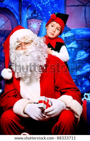 Santa Claus sitting with a little cute boy elf over Christmas background.