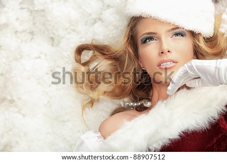 Beautiful young woman in Santa Claus clothes lying in snow.