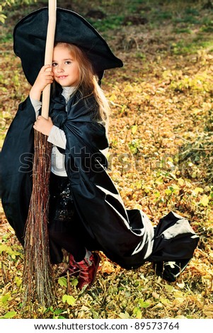 Shot of a little girl in halloween costume posing with broom and pumpkin outdoor.