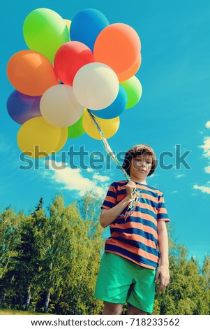 Portrait of a happy boy with many colorful balloons over blue sky. Summer holidays. Birthday.