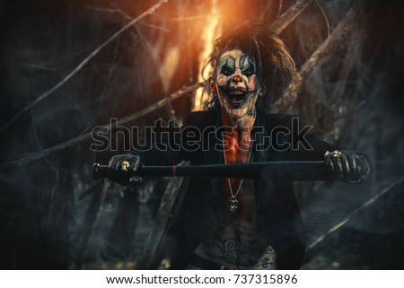 Scary punk clown man smeared with blood in a night forest. Halloween. Horror, thriller film.