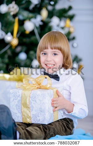 Cute five-year-old boy sits in a beautiful room near a Christmas tree with gift box. Luxurious apartments decorated for Christmas. Merry Christmas and Happy New Year.