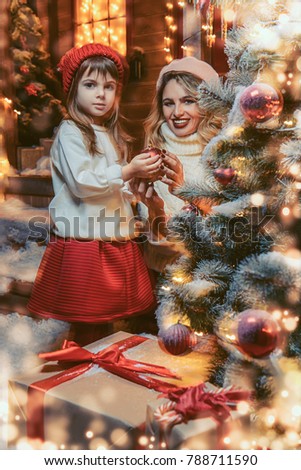 Happy mother and daughter decorate the Christmas tree  in the yard of their house. Merry Christmas and Happy New Year.