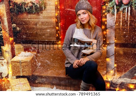 Happy girl in a warm winter clothes and skates in her hands, posing near the house decorated for Christmas. Time for miracles. Merry Christmas and Happy New Year.