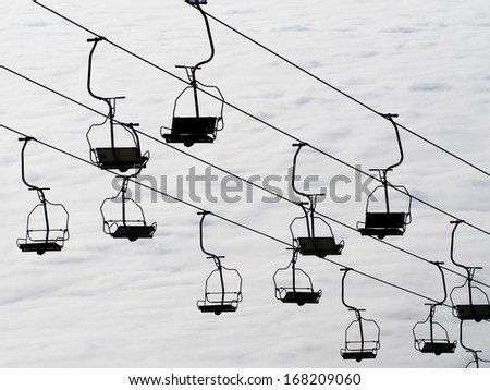 Ski lift chairs on bright winter day over the clouds