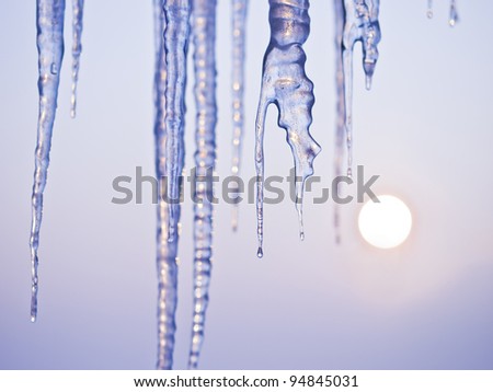 Thawing icicles isolated on blue with sun in background / face ice /