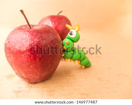 apple with a bite out of it showing a plasticine worm on brown paper background