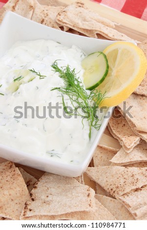 Tzatziki sauce made with yogurt, cucumbers, dill and lemon in a bowl with pita chips on the side