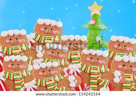 Pack of gingerbread men cookies in a winter wonderland wearing a scarf, while snowing with christmas tree in the background