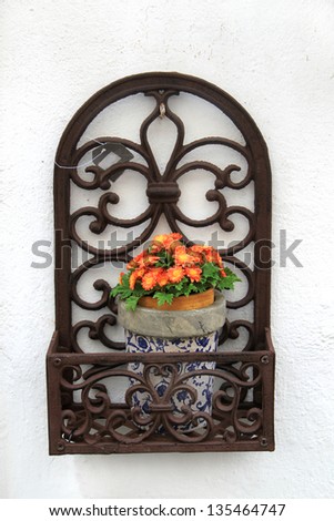 Decorative iron work flower pot holder with orange blossoms on a white stucco wall background, in Evora, Portugal