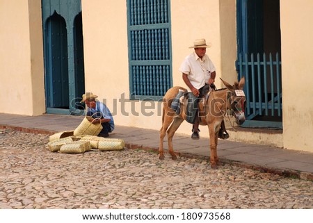 TRINIDAD,CUBA-FEBRUARY,25,2014: Two men on the cobblestone street of Trinidad, Cuba, one is weaving baskets and the other sits on a donkey