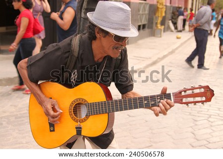 HAVANA,CUBA-FEB. 21,2014: A music man plays his guitar to tourists walking by downtown Havana Cuba