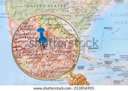 Blue tack on map of North America with magnifying glass looking in on Mexico City the capitol of Mexico