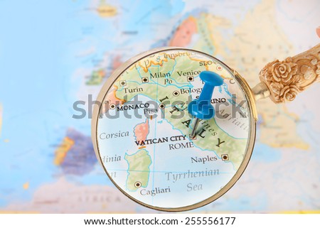Blue tack on map of Europe with magnifying glass looking in on Rome, and Vatican City, Italy