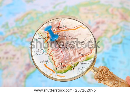 Blue tack on map of  the world with magnifying glass looking in on Sana, Yemen, Asia