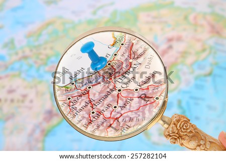 Blue tack on map of  the world with magnifying glass looking in on Tehran, Iran, Asia