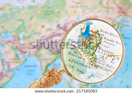 Blue tack on map of the world with magnifying glass looking in on Kuala Lumpur, Malaysia