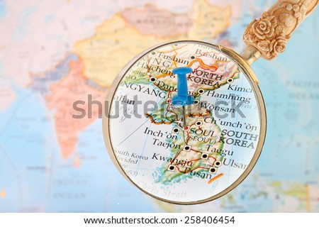 Blue tack on map of Asia with magnifying glass looking in Seoul, South Korea
