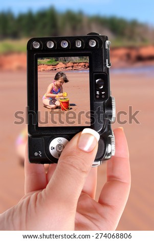 Woman taking a picture of little girl playing in the red sands of Prince Edward Island\'s Cabot Beach