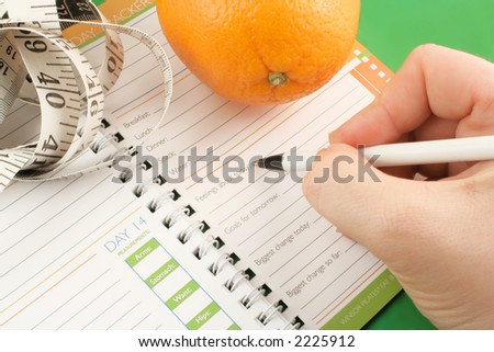 writing in a diet and nutrition journal with orange and tape measure to the side