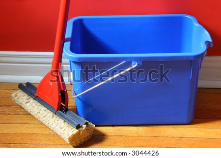 mop and blue bucket on hardwood floors with red wall in background