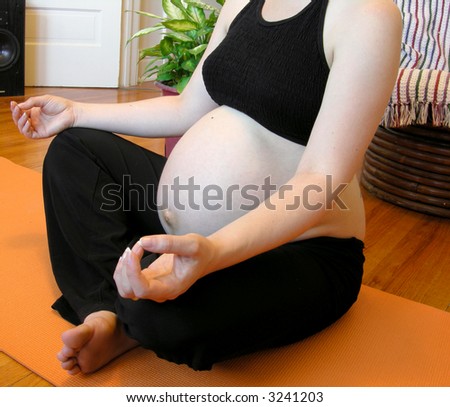 bare belly woman doing mediative yoga at nine months of pregnancy