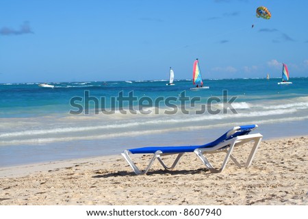empty beach chair overlooking the ocean with boats on the Caribbean shore of Bavaro beach, Punta Cana in the Dominican Republic
