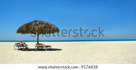 woman relaxing on a lounger reading a book at a tropical beach panorama