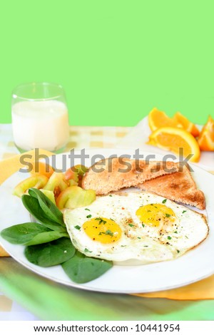 two sunny side up eggs on plate with fresh vegetables whole wheat toast and sliced orange in the background