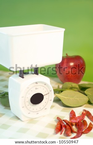 white food scale stating that something inside weighs 4 grams, apple, spinach and jalapeno peppers are on table beside it