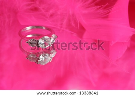 glamorous diamond ring on vanity mirror with a pink feather boa in the background appropriate for invitations with copyspace