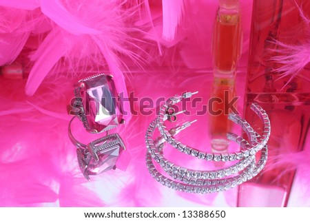 glamorous diamond ring and earring on vanity mirror with a pink feather boa and perfume bottles in the background
