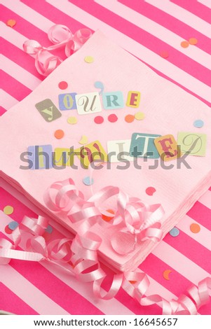 cut out letters spelling you\'re invited on pink napkins with curled ribbons and confetti, great for invitation cards