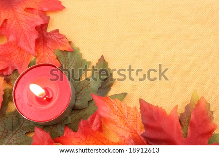 autumn leaf background or border frame  in orange, red, and green with lit tea light candle