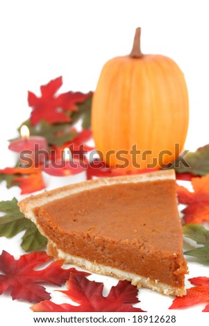 one piece of pumpkin pie on white plate surrounded by fall leaves,tea lights, and pumpkin in the background