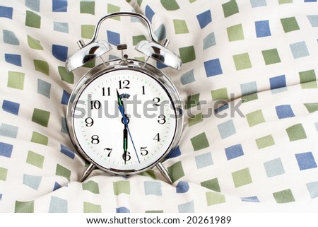 alarm clock resting on a pillow showing 11:30 at night, time to go to bed, or late lazy morning