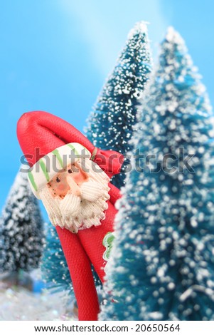 winter scene in glitter, Santa Claus is playing hide and go seek, peeking or hiding  behind miniature pine trees