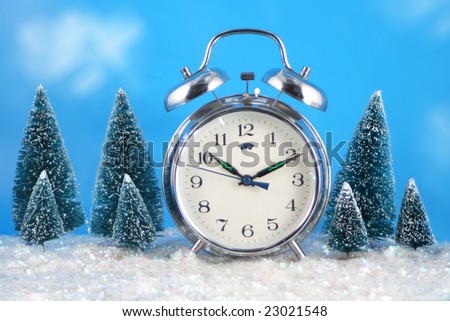 Conceptual image of \'wintertime\' with alarm clock,snow, and pine trees with blue sky