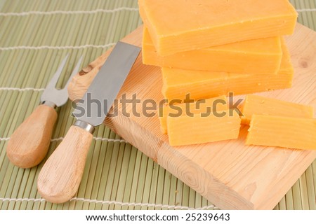 blocks of cheddar cheese on a wooden block with cheese cutting knife and accessories