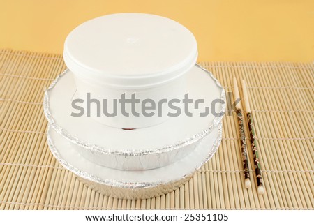 chinese food delivery or takeout aluminum covered containers and cardboard boxes on bamboo placemat