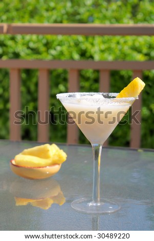 Enjoying the backyard with a pina colada and pineapple garnish on a glass patio table, green trees on background (short depth of field)
