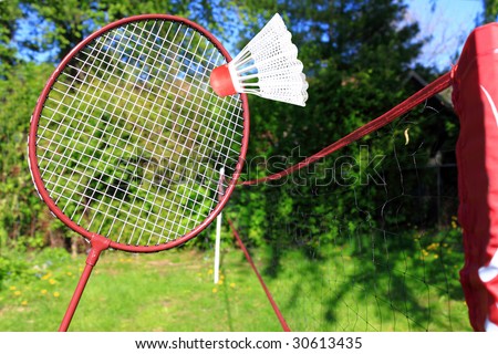 Playing the sport of badminton in the backyard, red racquet is about to hit shuttle in the air over the net