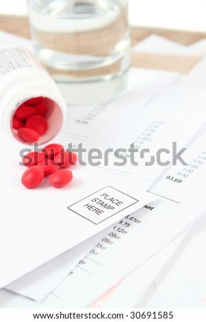 Different bills to be paid and envelopes with red pills and water to soothe the headache of paying bills