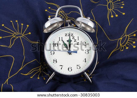 alarm clock resting on a pillow showing 11 o\'clock, time to go to bed with zzzzz as 12 o\'clock