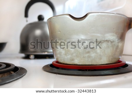 Boiling water in glass pot on stove with kettle in the background (shallow depth of field)