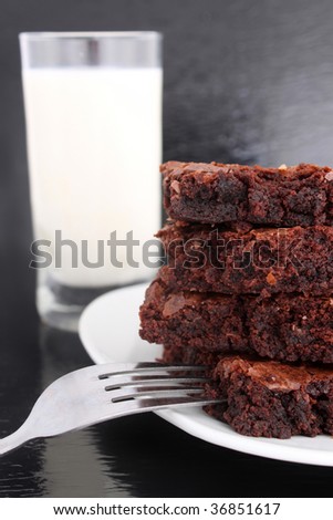 Chocolate fudge brownies on black with glass of milk in the background and a fork on the plate