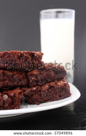 Pile of chocolate fudge brownies on a plate with a glass of milk in the  background (short depth of field)