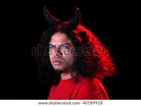 Angry man dressed as the devil with horns and  red creative lighting shining on his long curly black hair
