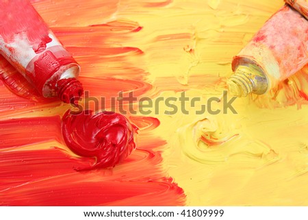 Red and yellow colors of artist\'s oil paints spilling out into a smudged painted background