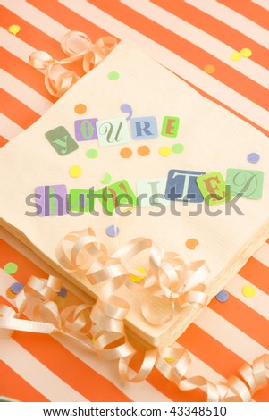 cut out letters spelling you\'re invited on beige napkins with curled ribbons and confetti, great for invitation cards on an orange striped background